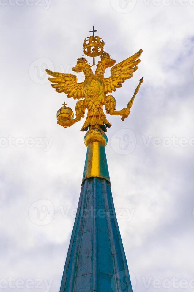 Golden coat of arms, two-headed eagle, of Russian Federation on the top of Kremlin tower against of a gray overcast sky photo