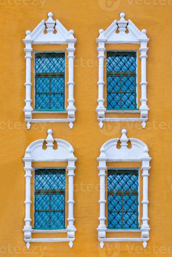 Close up view on a facade of ancient orange building with four windows with lattice and carved white stone platbands as texture photo