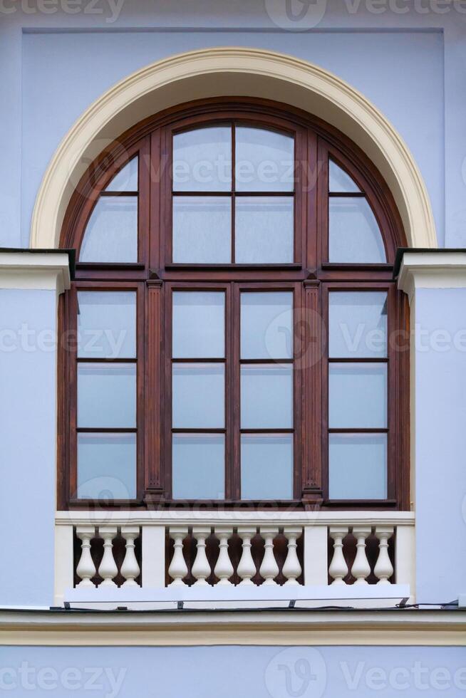 Close up view on a arched window with wooden frame and decorative white fence on bottom on a facade of blue ancient building photo
