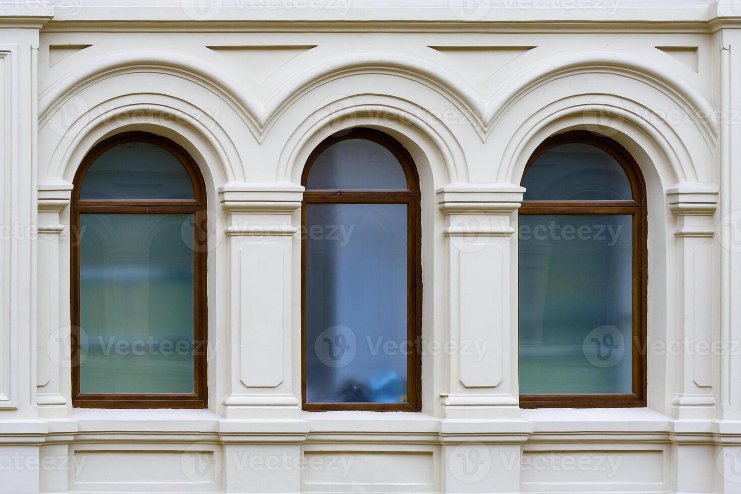 Front view on a facade of ancient stone building with three arched windows with carved platbands photo