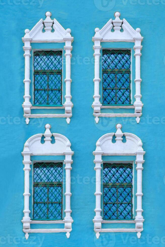 Close up view on a facade of ancient blue building with four windows with carved white stone platbands as texture photo