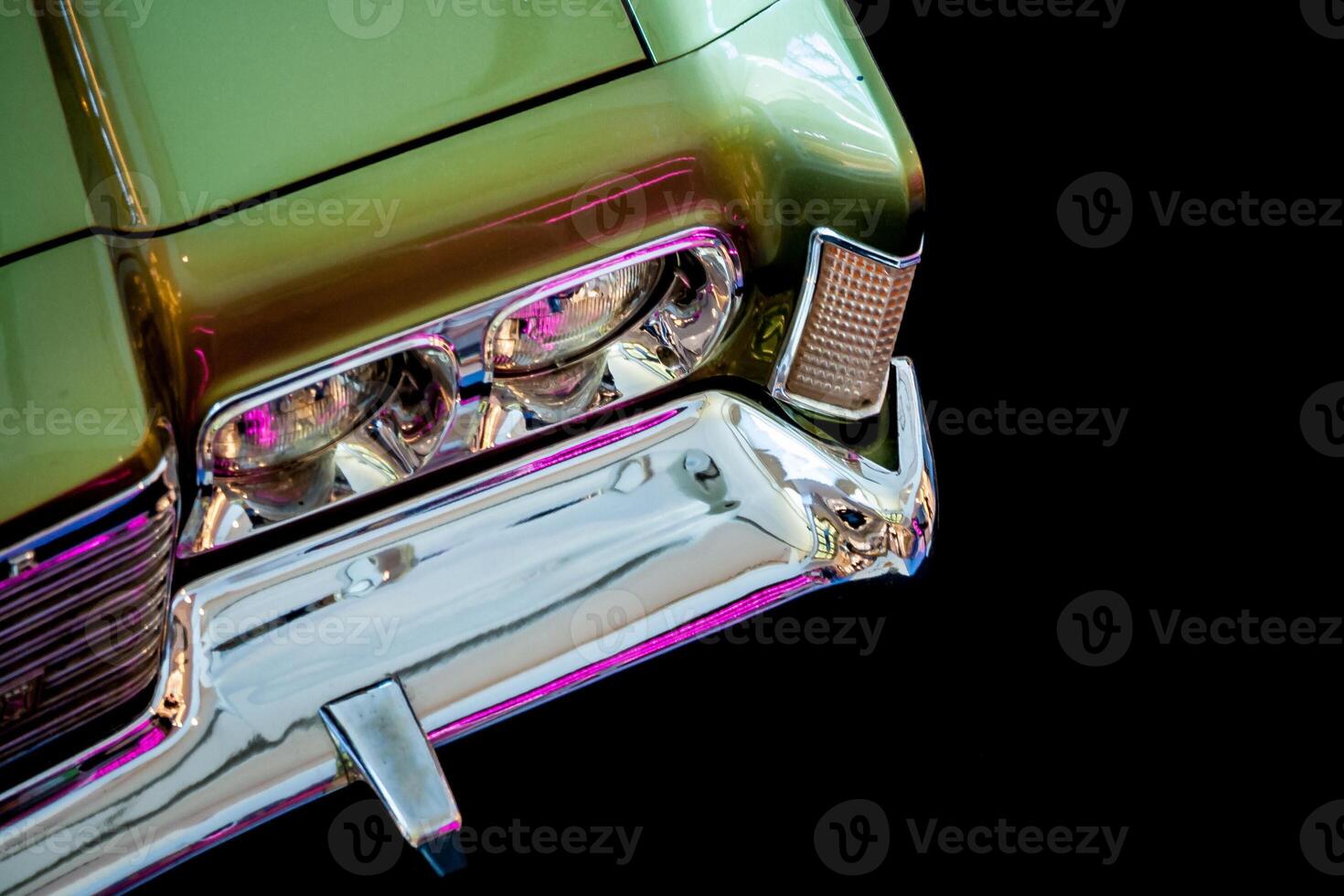 Exhibition of retro cars. Fragment of a green car's headlamp lit by a purple light on a black background photo