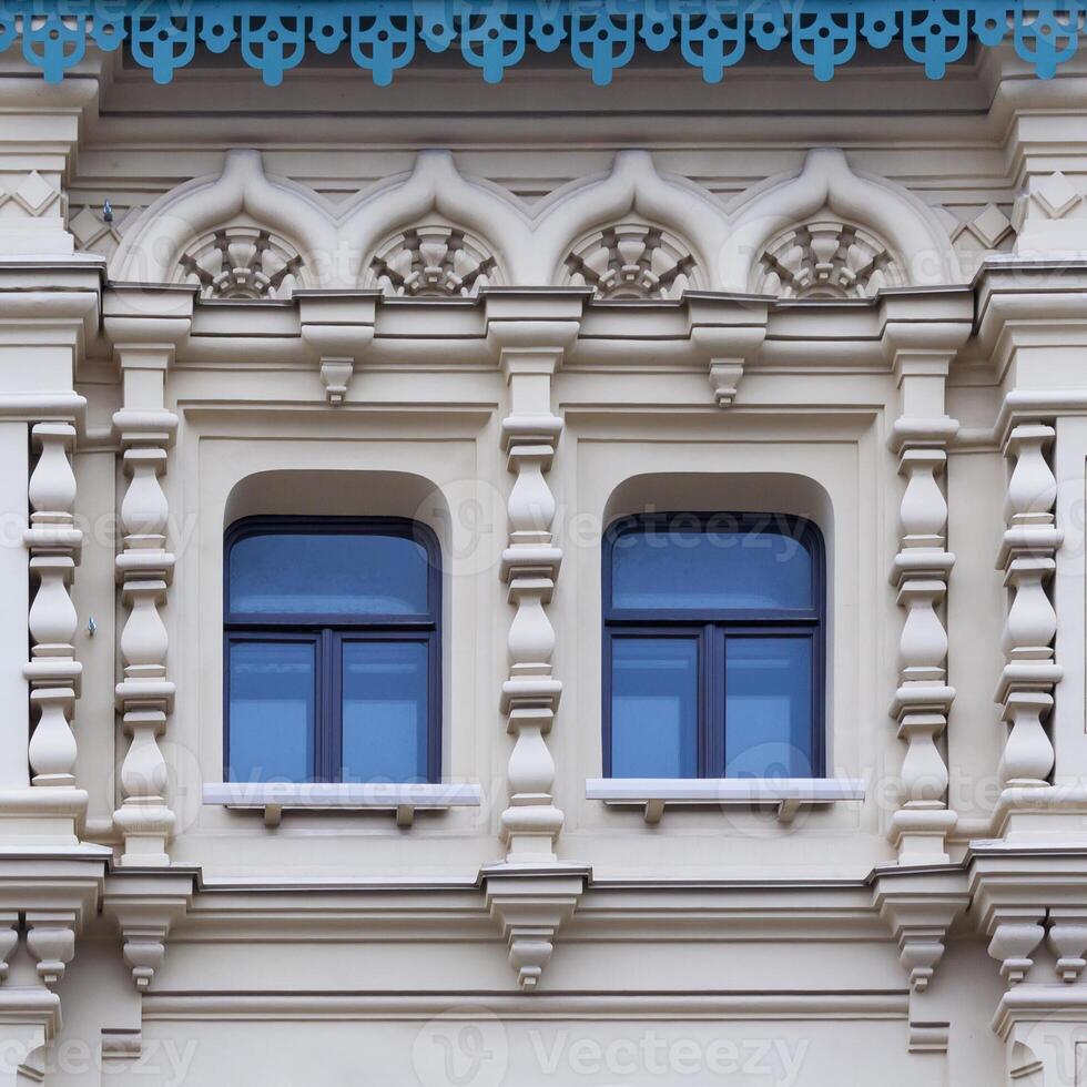 Close up view on a facade of white ancient building with decorative ornaments and two windows photo