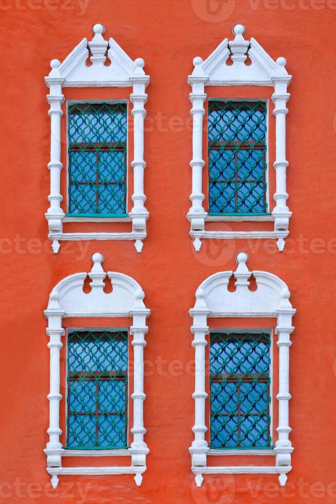 Close up view on a facade of ancient red building with four windows with carved white stone platbands as texture photo