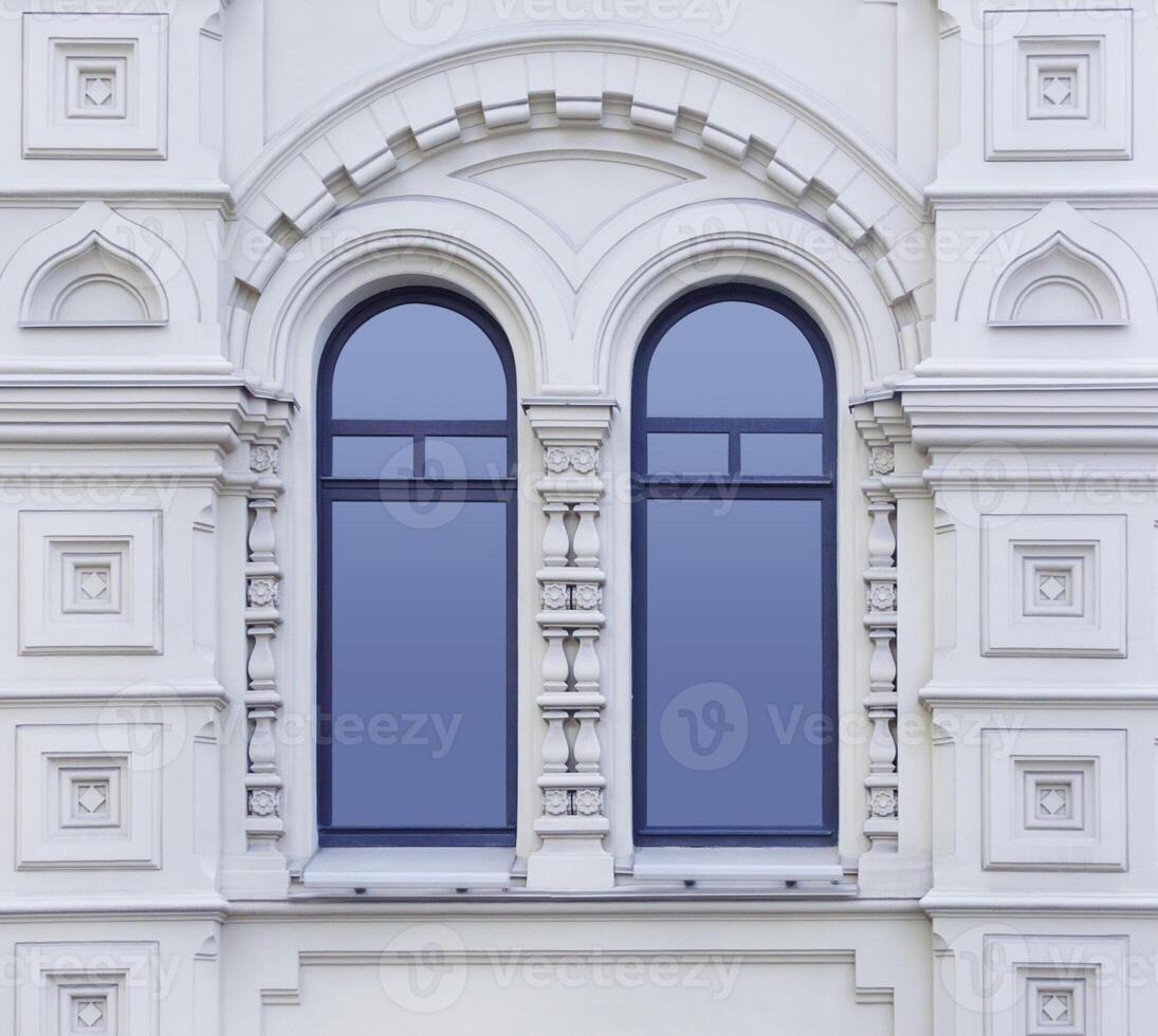 Close up view on a facade of white ancient building with decorative ornaments and two-part arched windows as texture photo