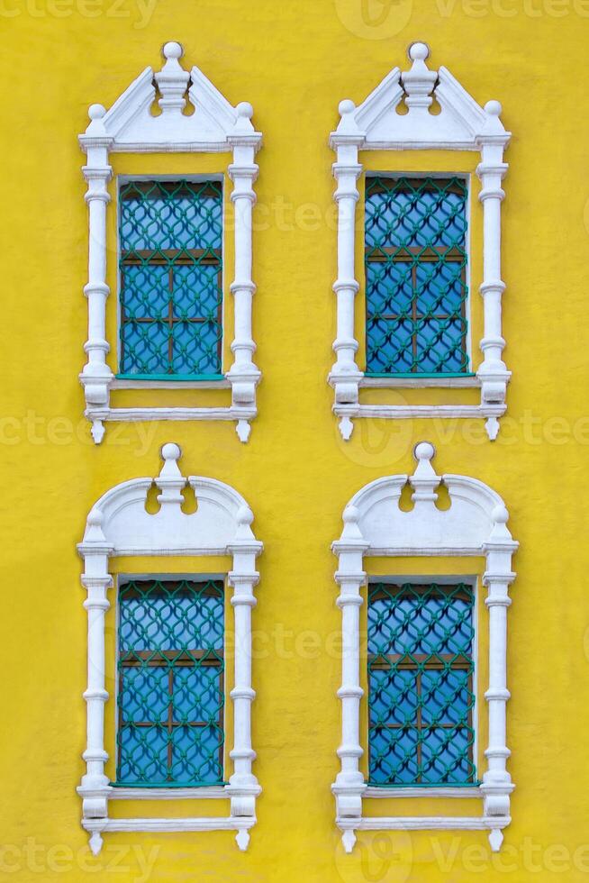 Front view on a facade of ancient yellow building with four windows with carved white stone platbands as texture photo