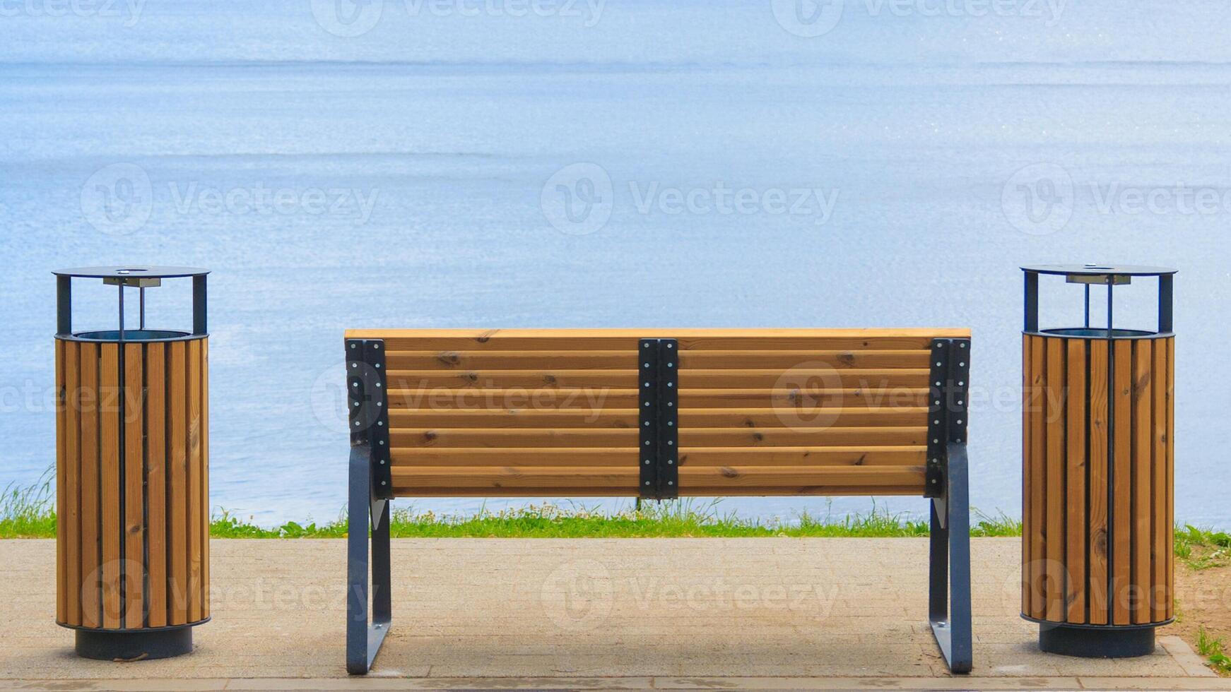 Rear view of a wooden bench with garbage cans facing the blue water with copy space photo