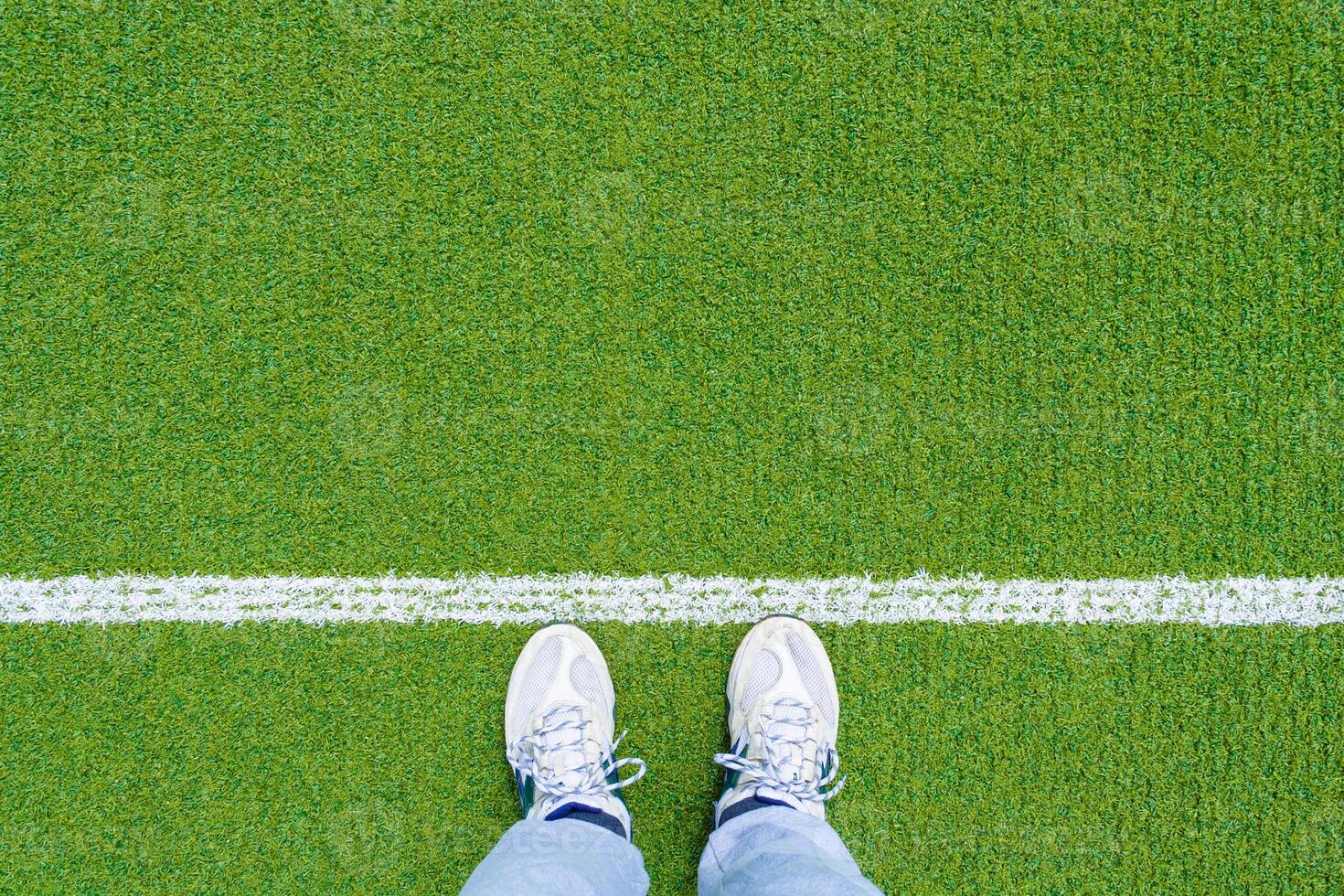 Top view of legs in sports shoes in front of the white line on the green sports ground with copy space photo