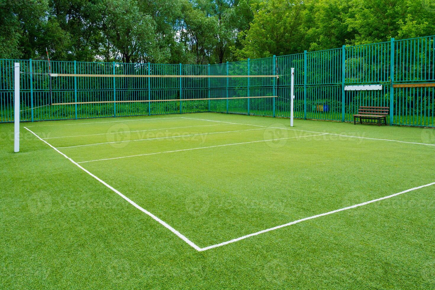 The sports playground in the park with artificial grass and a stretched net on a background of green trees photo