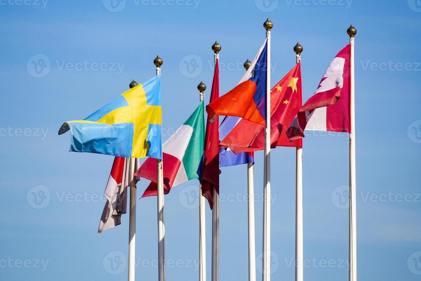 Flags of different countries flutters in the wind against a light blue sky photo