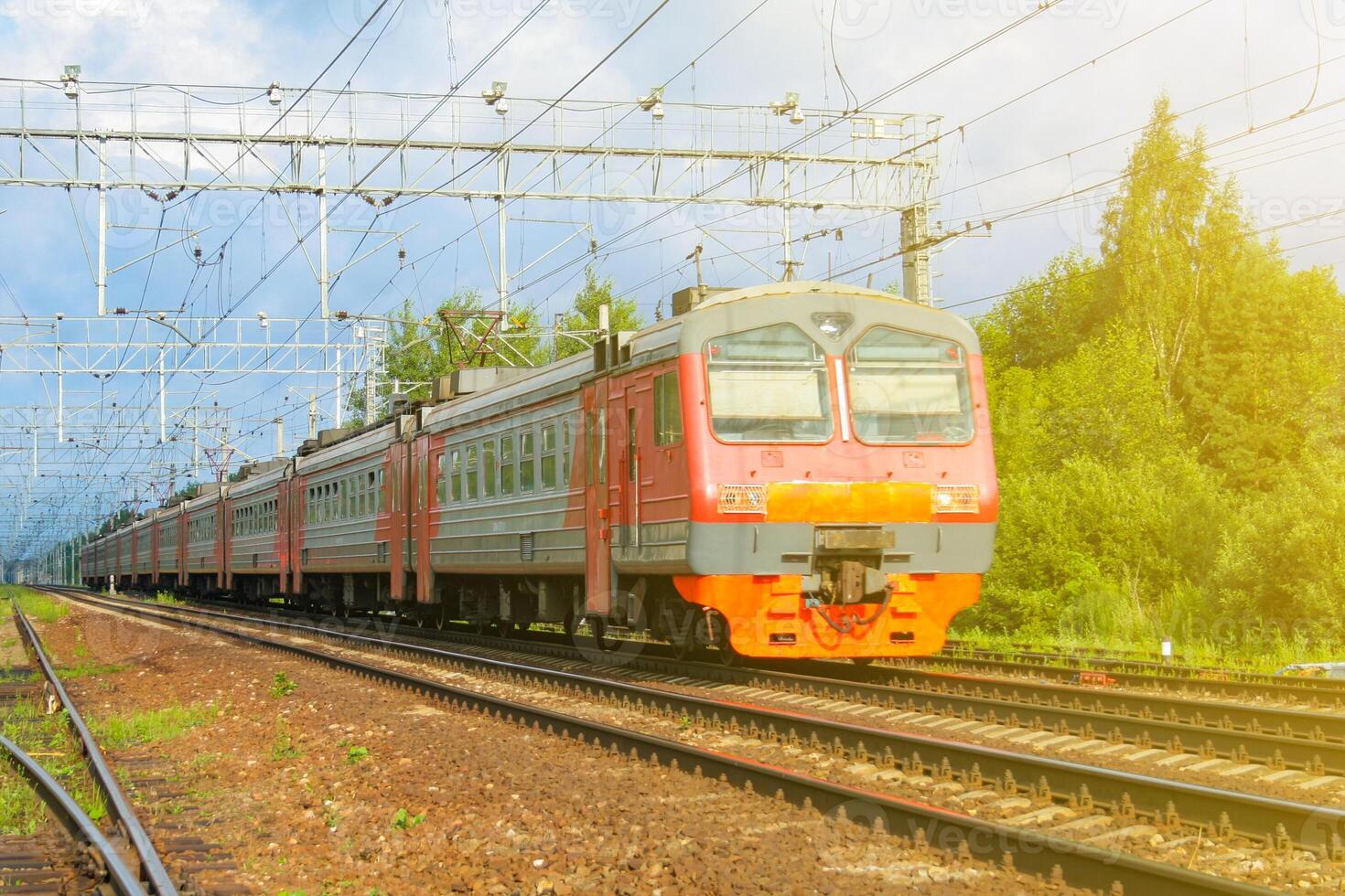 Passenger electric train, illuminated by sunlight moves against the background of green forest photo