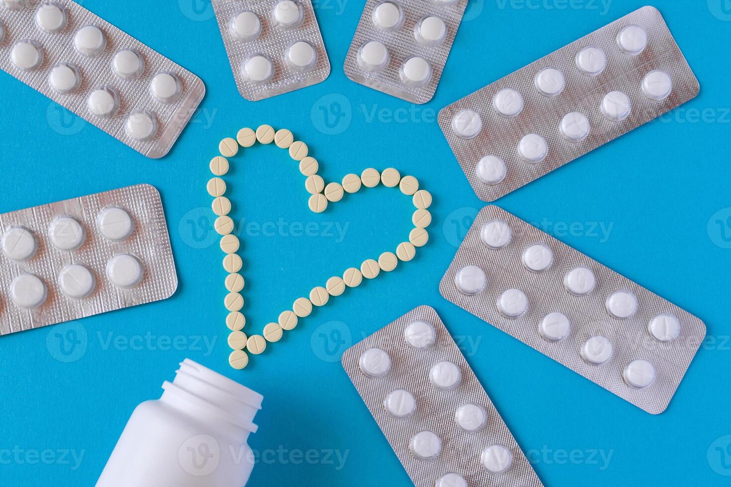 Yellow tablets are laid out in the shape of a heart, white jar surrounded by a pills in blisters on a blue background photo