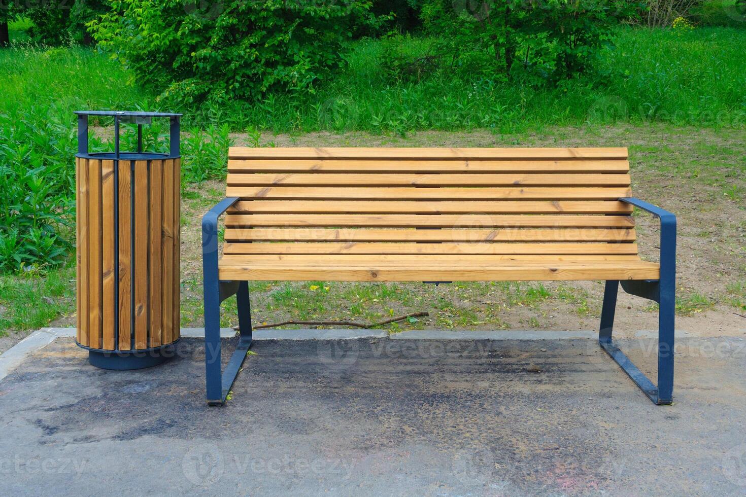 Wooden bench with metal legs and trash can in the park on a green lawn background photo