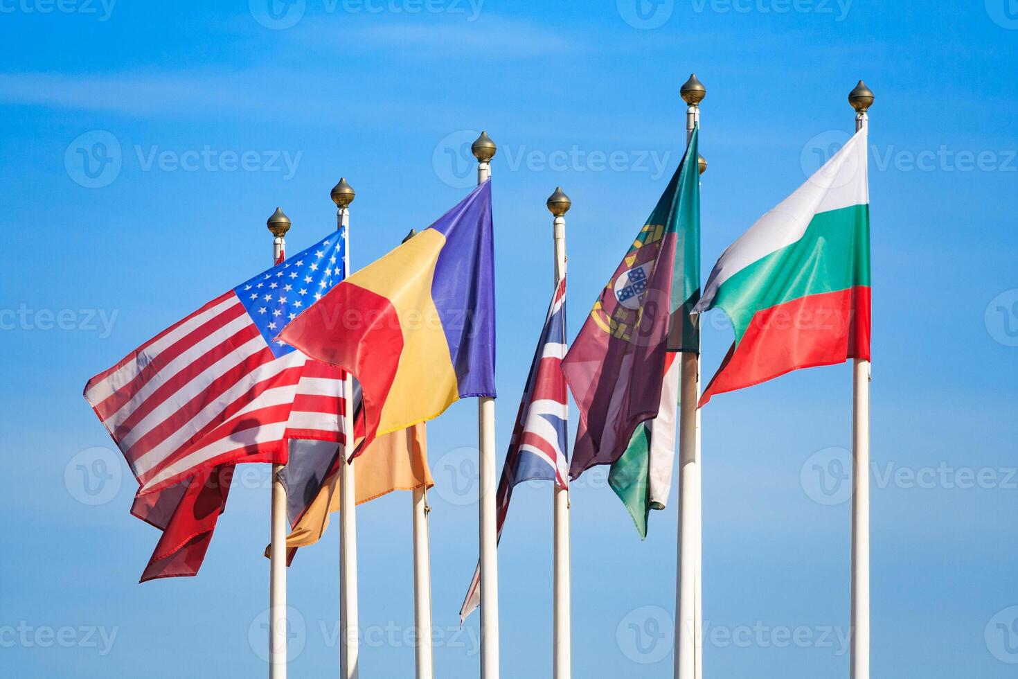 Close up view of a flags of different countries flutters in the wind against a blue sky photo