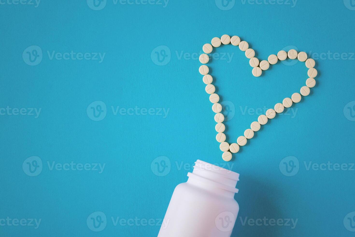 Yellow tablets are laid out in the shape of a heart and white jar on a blue background with copy space photo