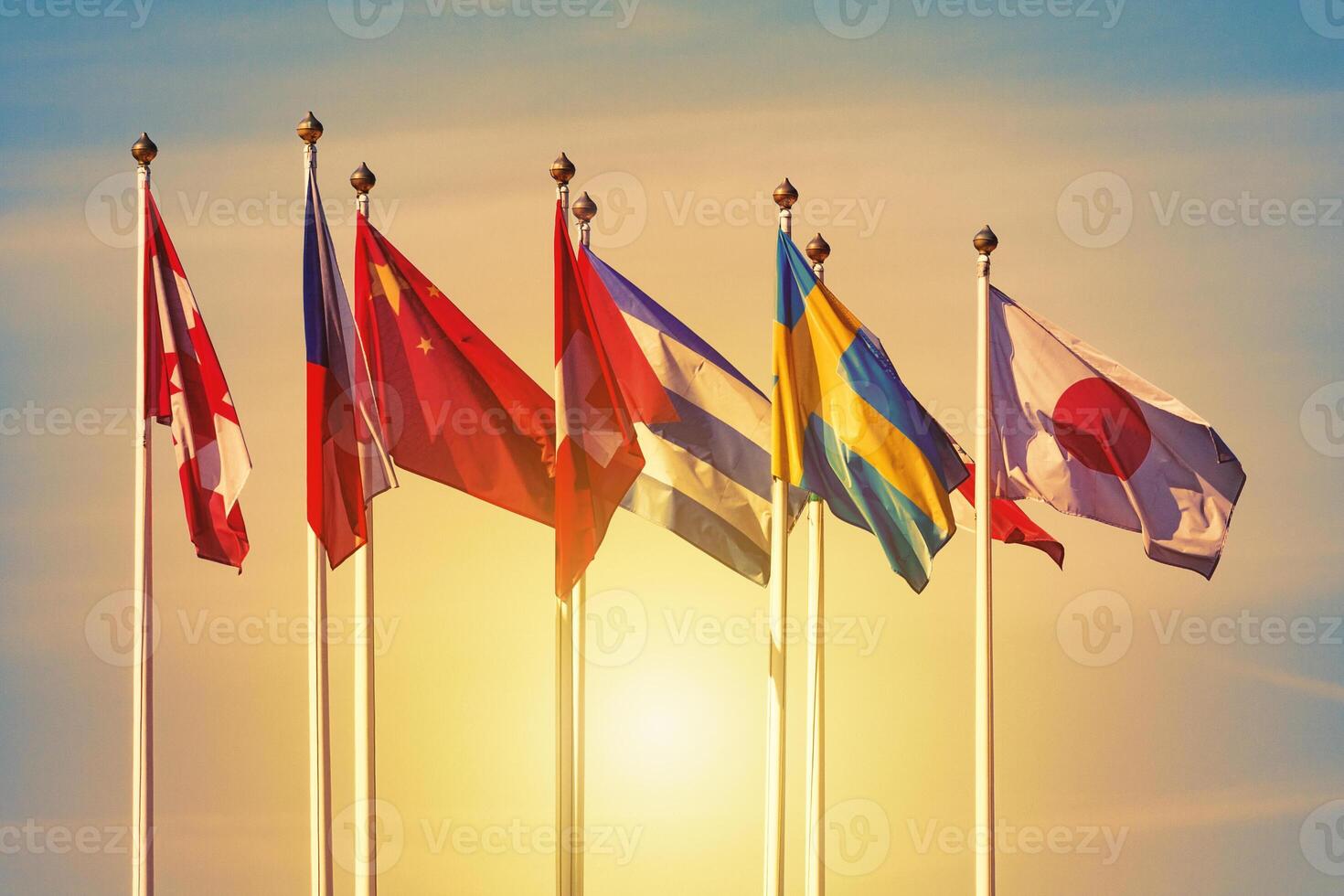 Flags of different countries on the white flagpoles against a sunset sky photo