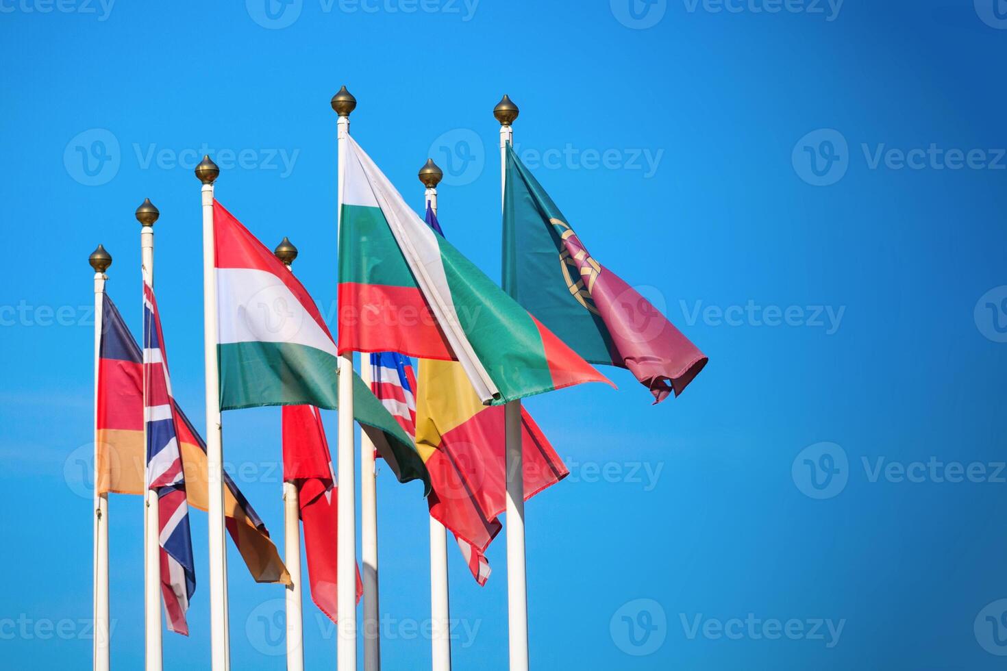 Flags of different countries develop in the wind against a bright blue sky with copy space photo