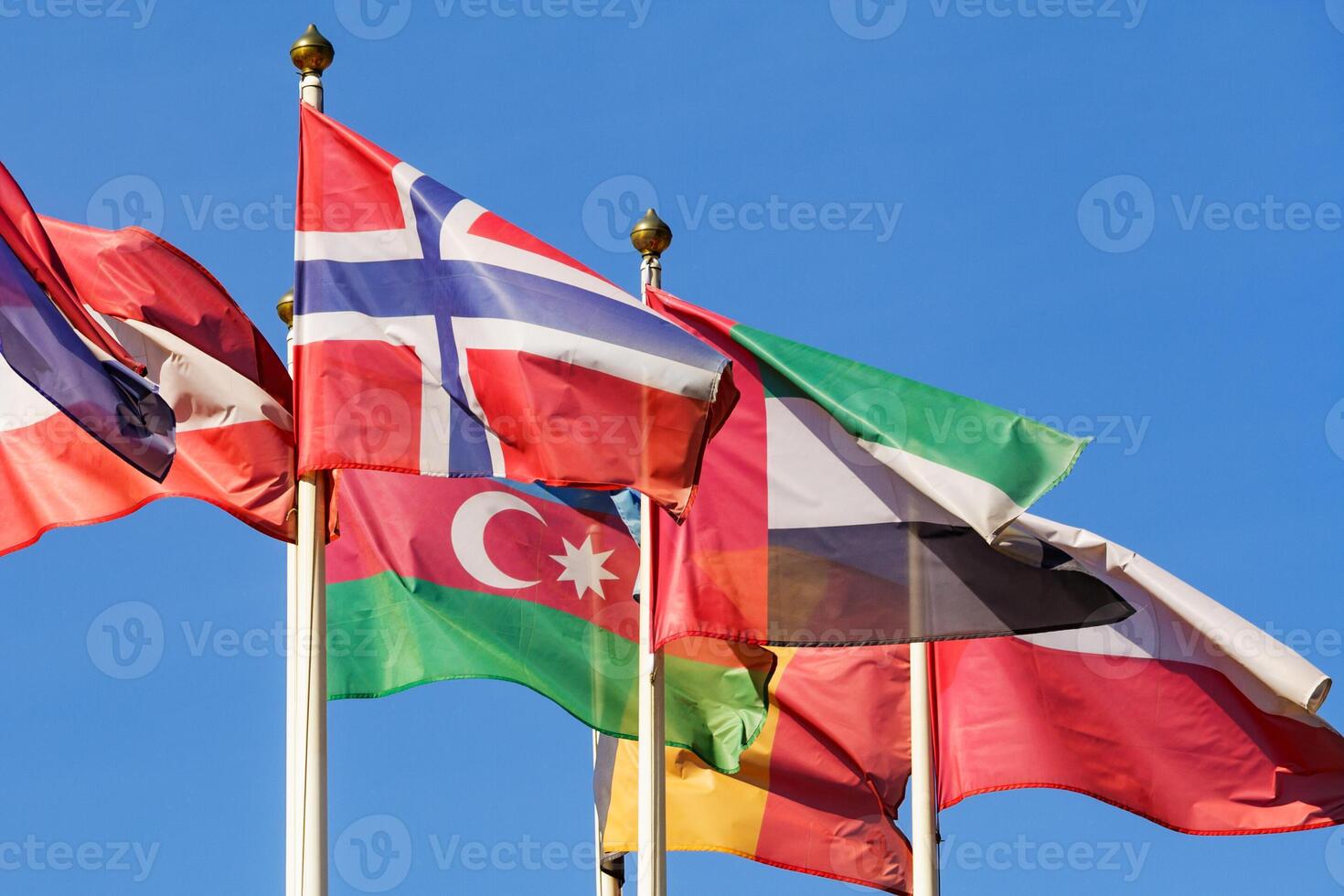 Close up view of a flags of different countries flutters in the wind against a clear blue sky photo