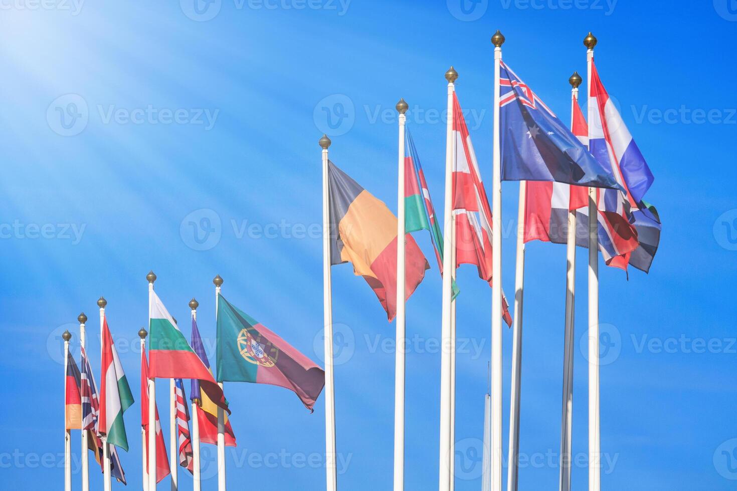 Flags of different countries illuminated by the rays of the sun against a bright blue sky photo