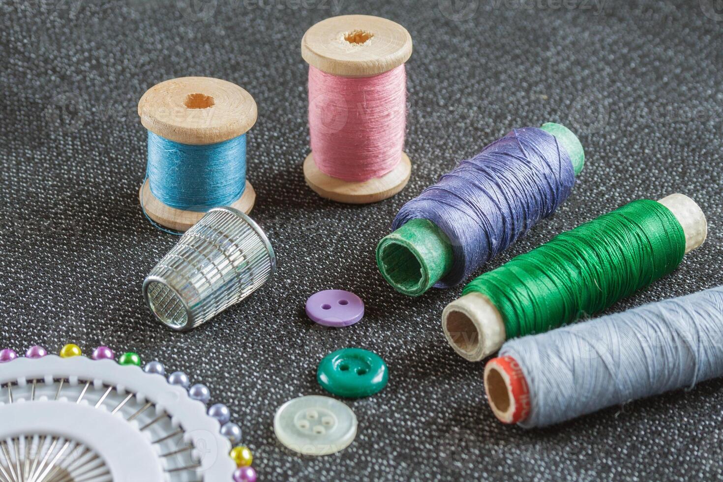 Sewing accessories spools of threads, needles, thimble, buttons on the textured fabric surface photo