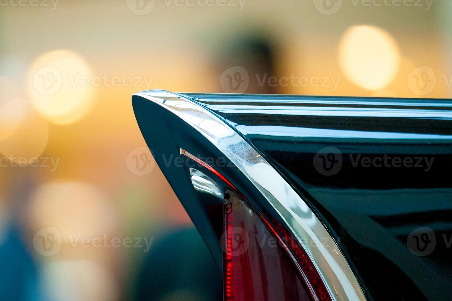 Fragment of a tail light of a black retro car against a background of orange lights in a blur photo