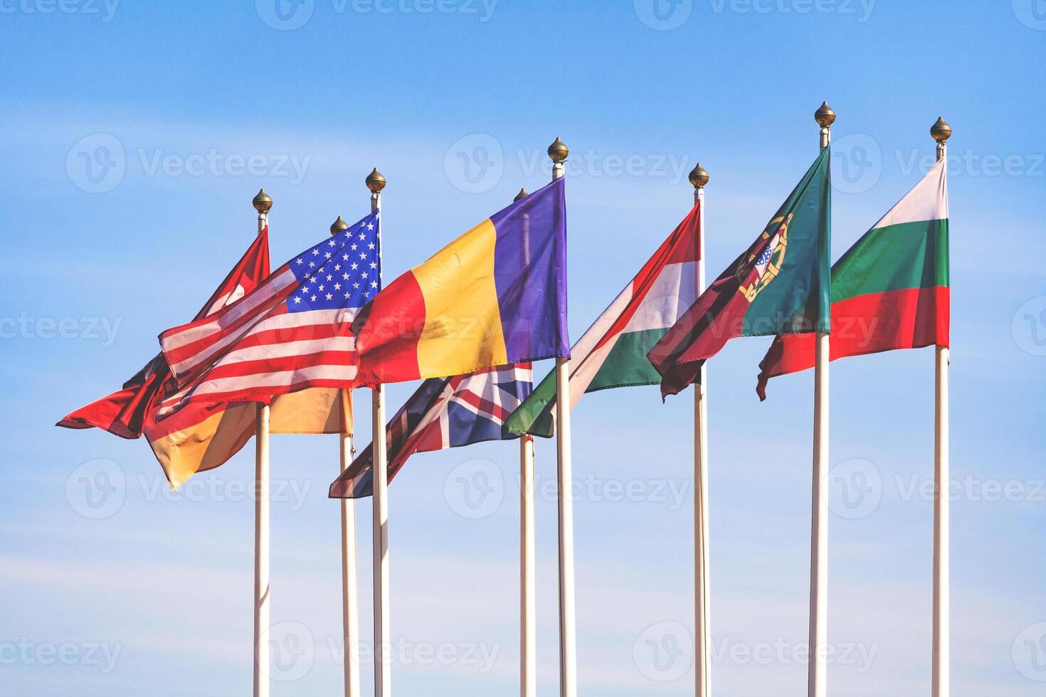 Flags of different countries flutters in the wind against a blue sky with clouds photo