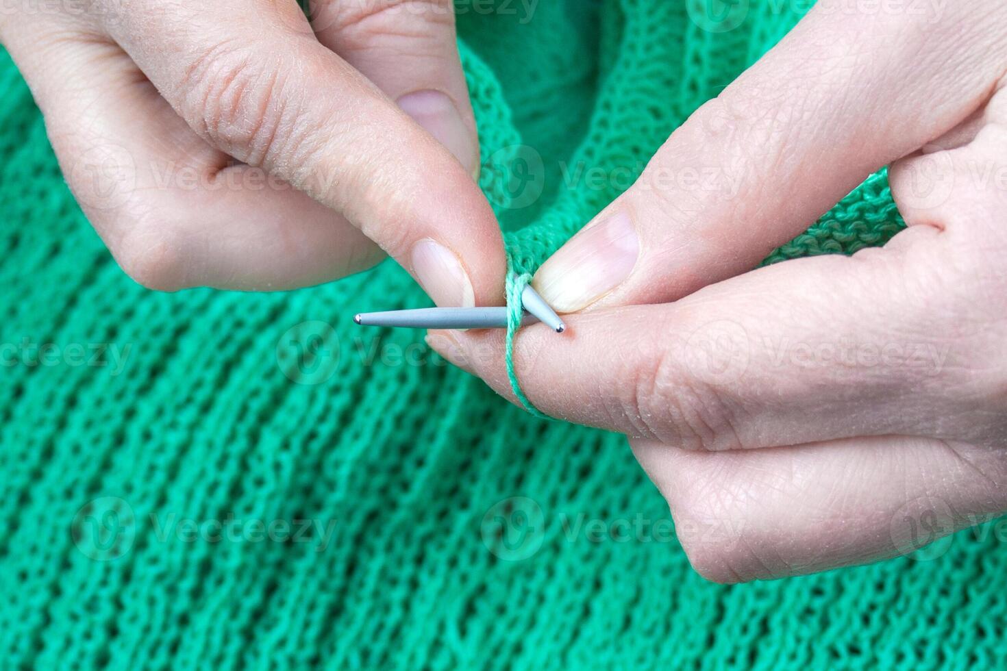 Close up view of a elderly woman hands who knits a green sweater photo