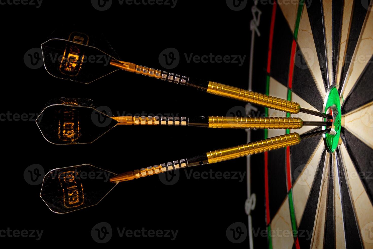 Sisal dartboard with three darts in a bullseye on a black background photo