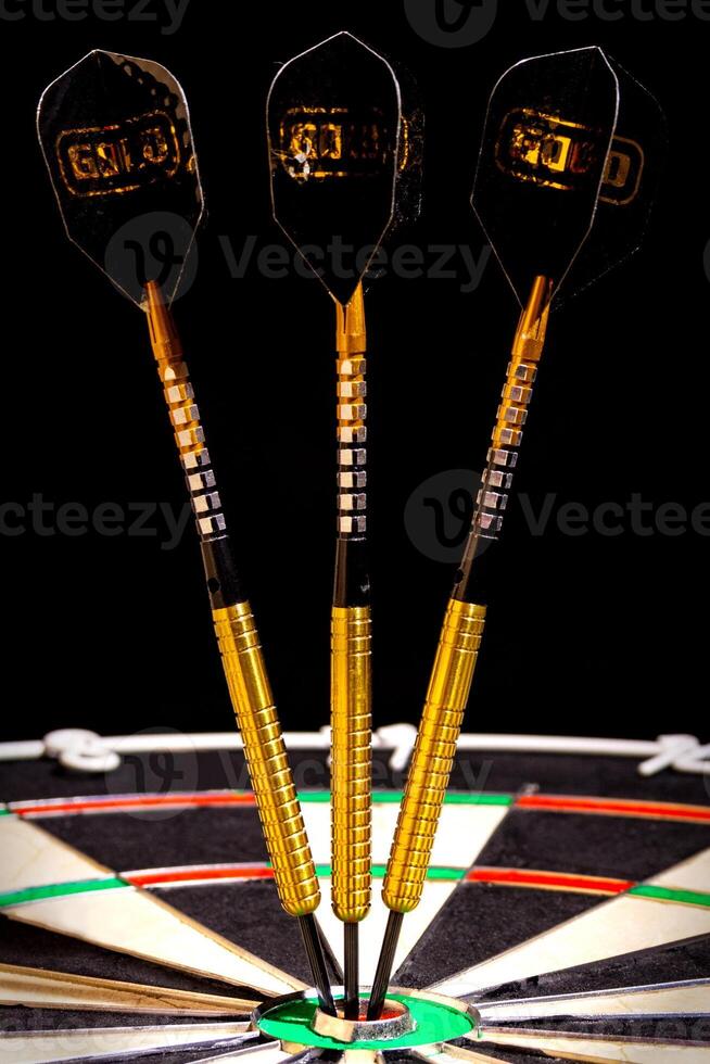 Sisal dartboard with three darts in a bullseye on a black background photo