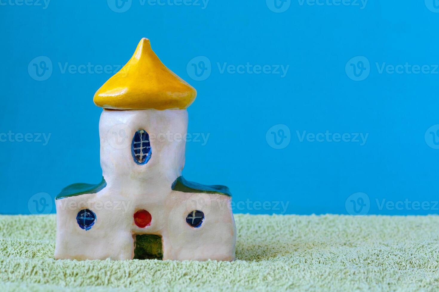 Miniature, hand-made by a child, ceramic church on a green look as grass surface, on a background of blue sky with copy space photo