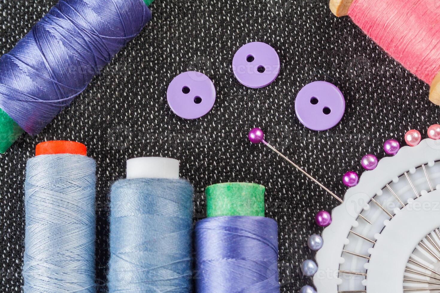 Sewing accessories spools of threads, needles, buttons, on the textured fabric surface photo