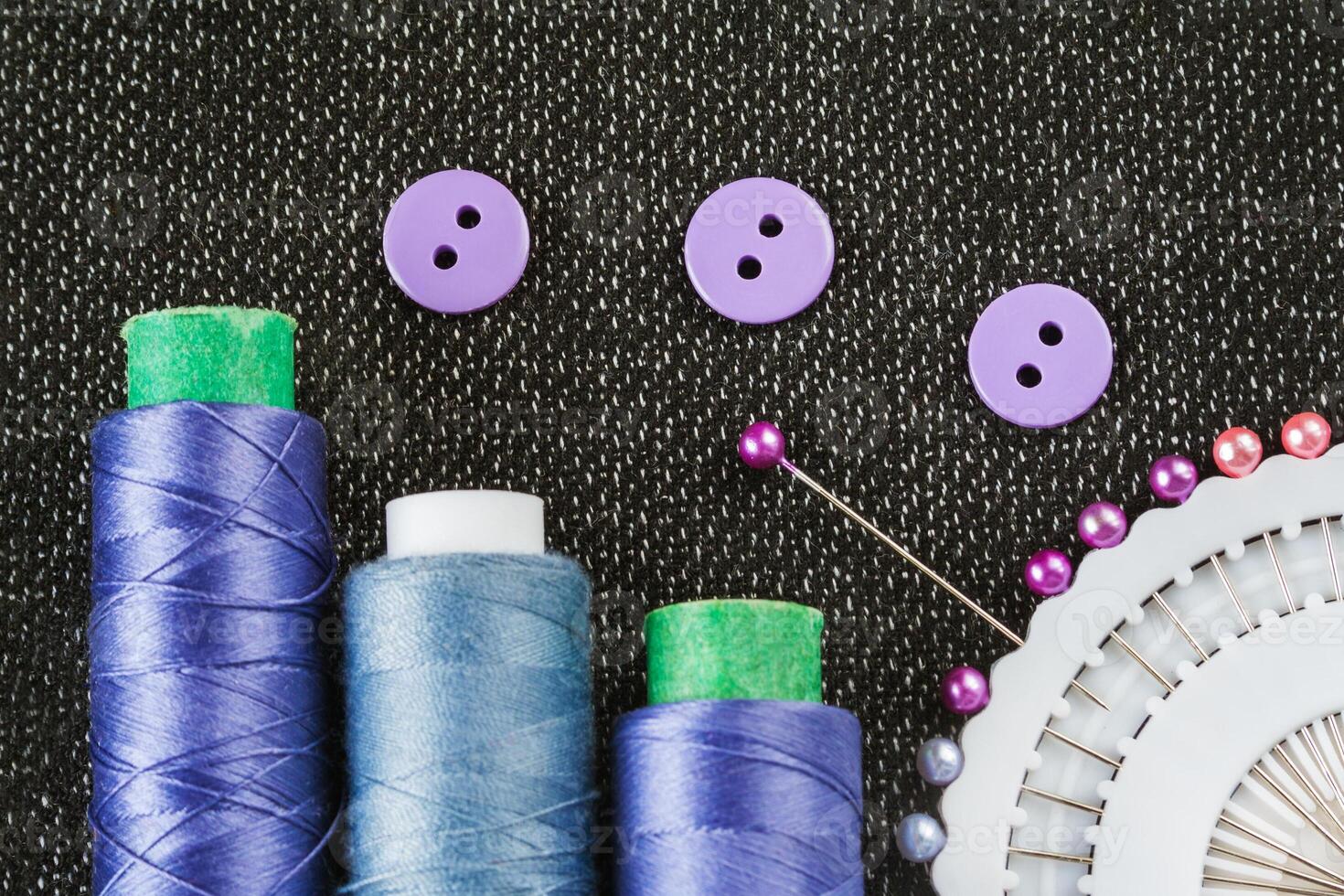 Sewing accessories spools of threads, needles, buttons, on the textured fabric surface photo