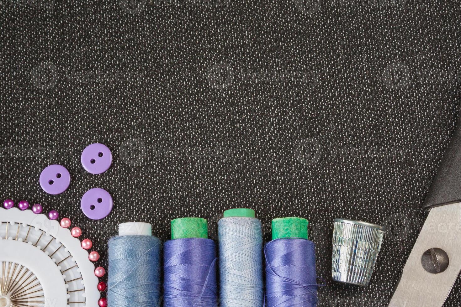 Sewing accessories spools of threads, needles, scissors, buttons on the textured fabric surface. Flat view with copy space photo