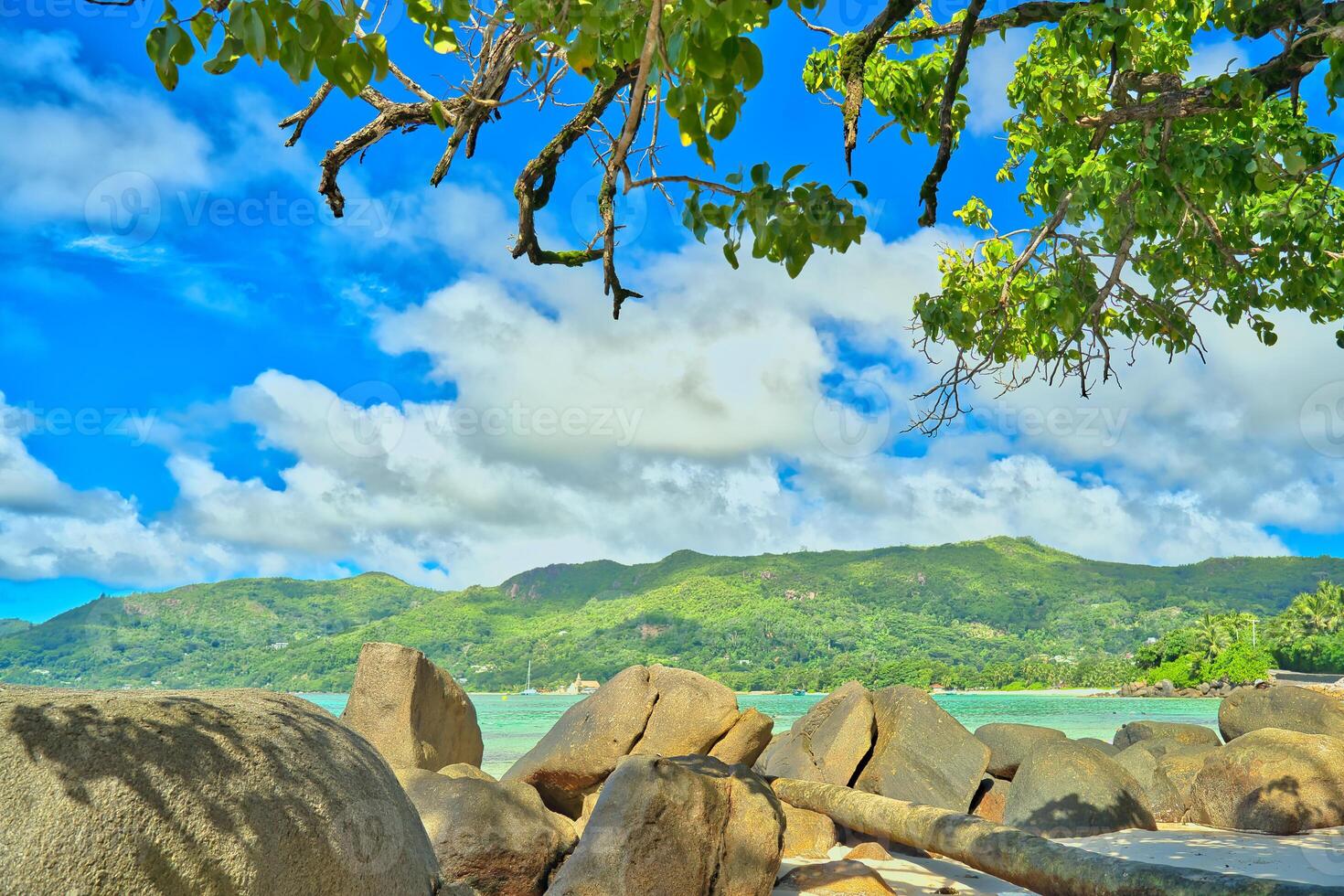 Anse royale beach, Mahe, blue sky turquoise water, low tide sunny day, white sandy beach and granite rock boulders, Seychelles mountain in the background photo