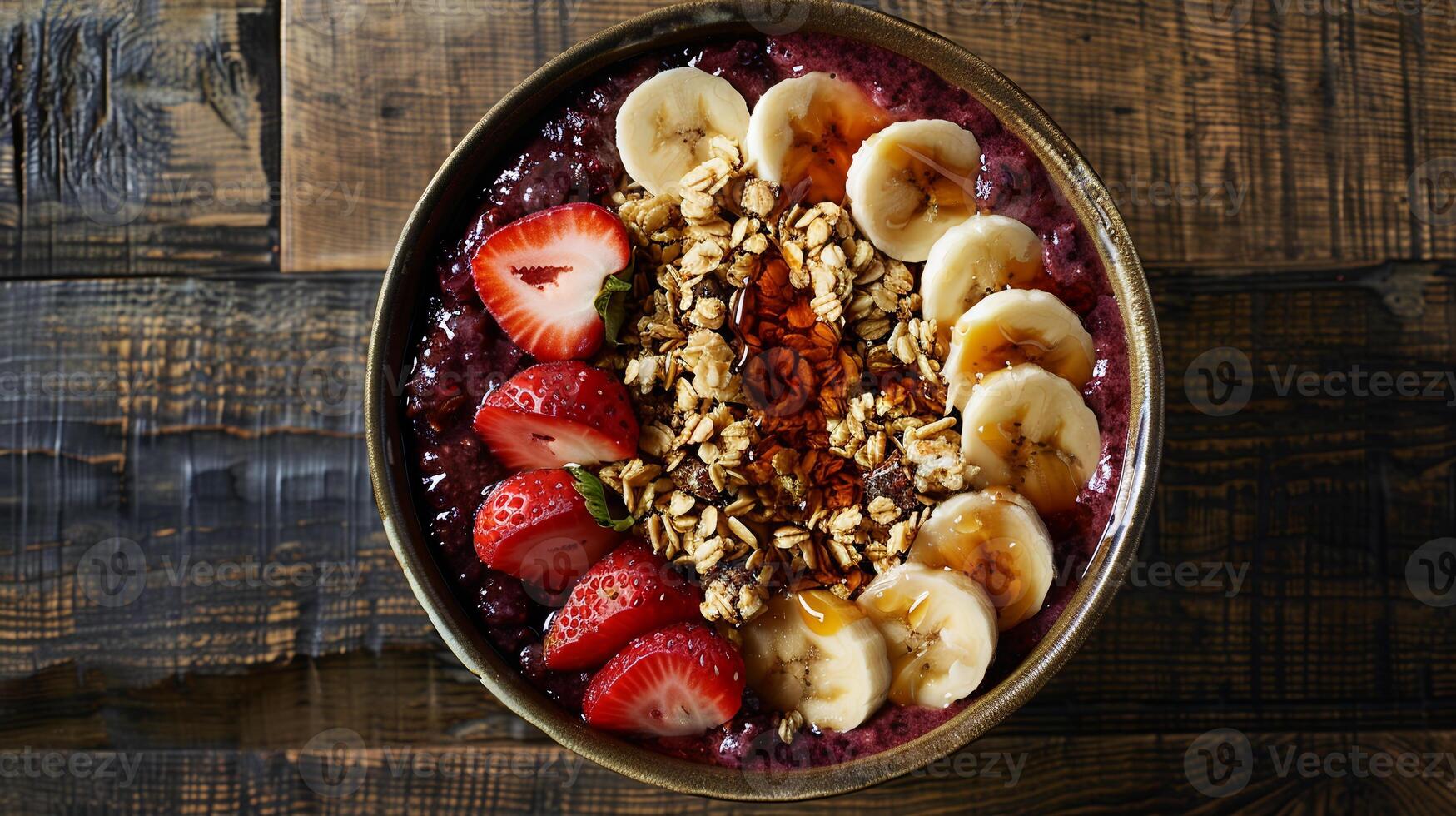 Acai bowl topped with granola, sliced bananas, strawberries, and a drizzle of honey. photo