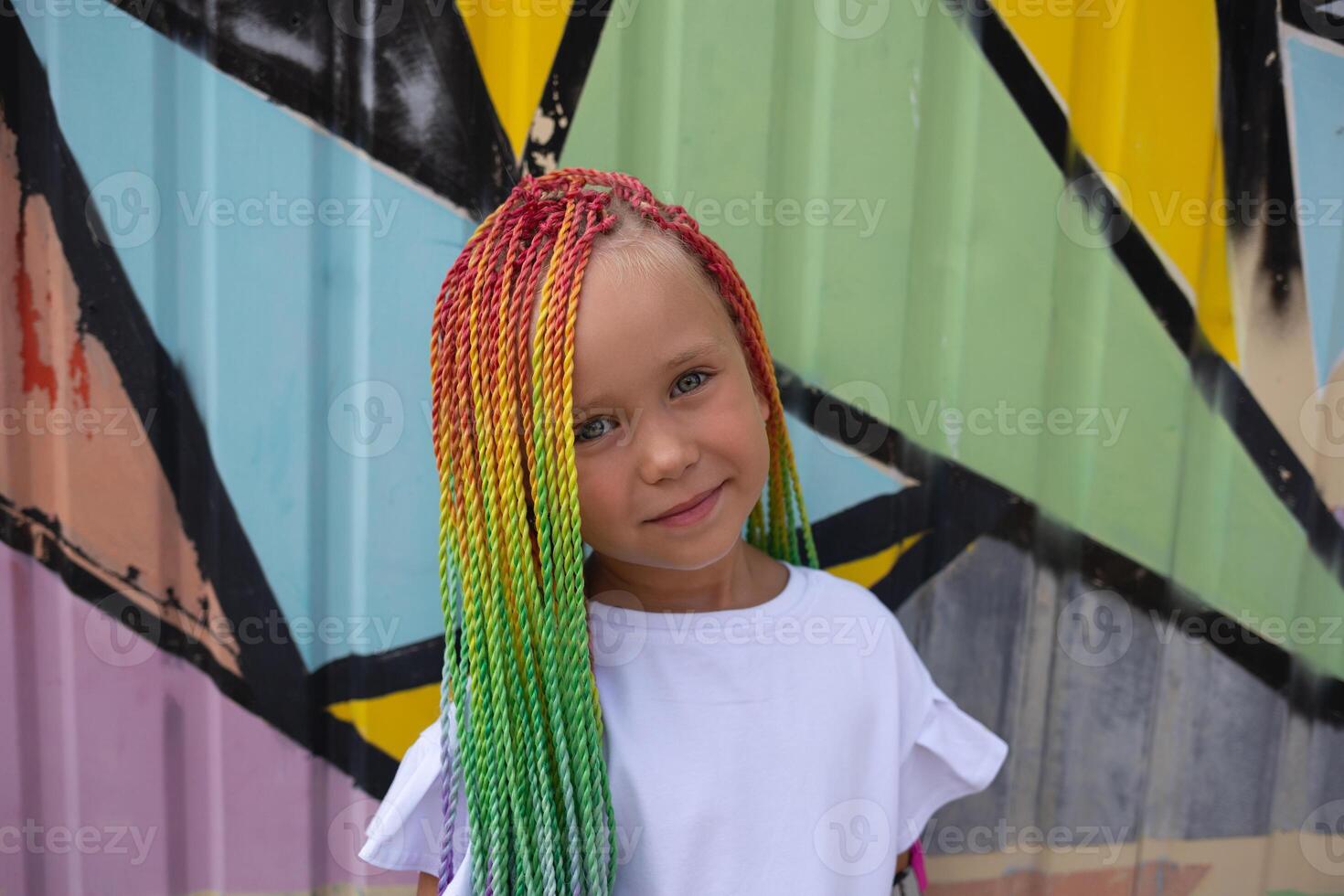 portrait of a little beautiful girl with multi-colored african braids on the background of a colorful wall photo
