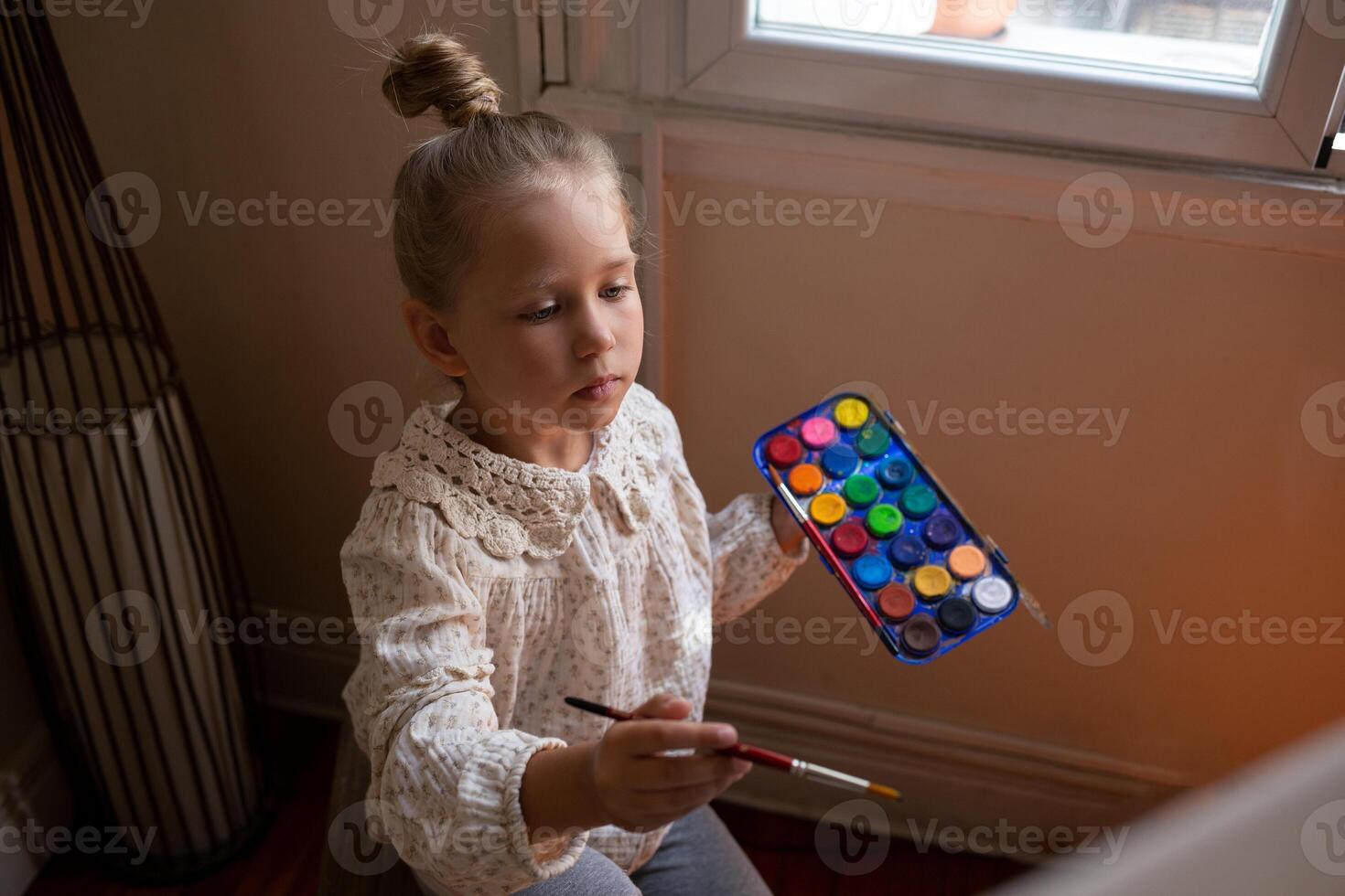 little cute girl draws with paints on canvas at the easel photo