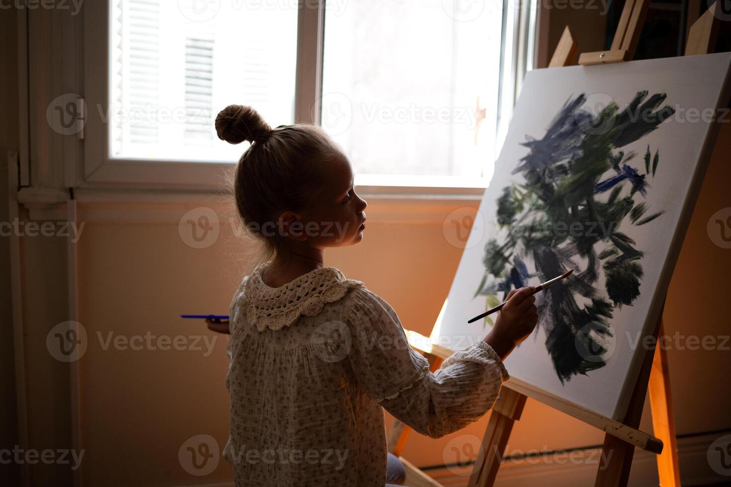 little cute girl draws with paints on canvas at the easel photo