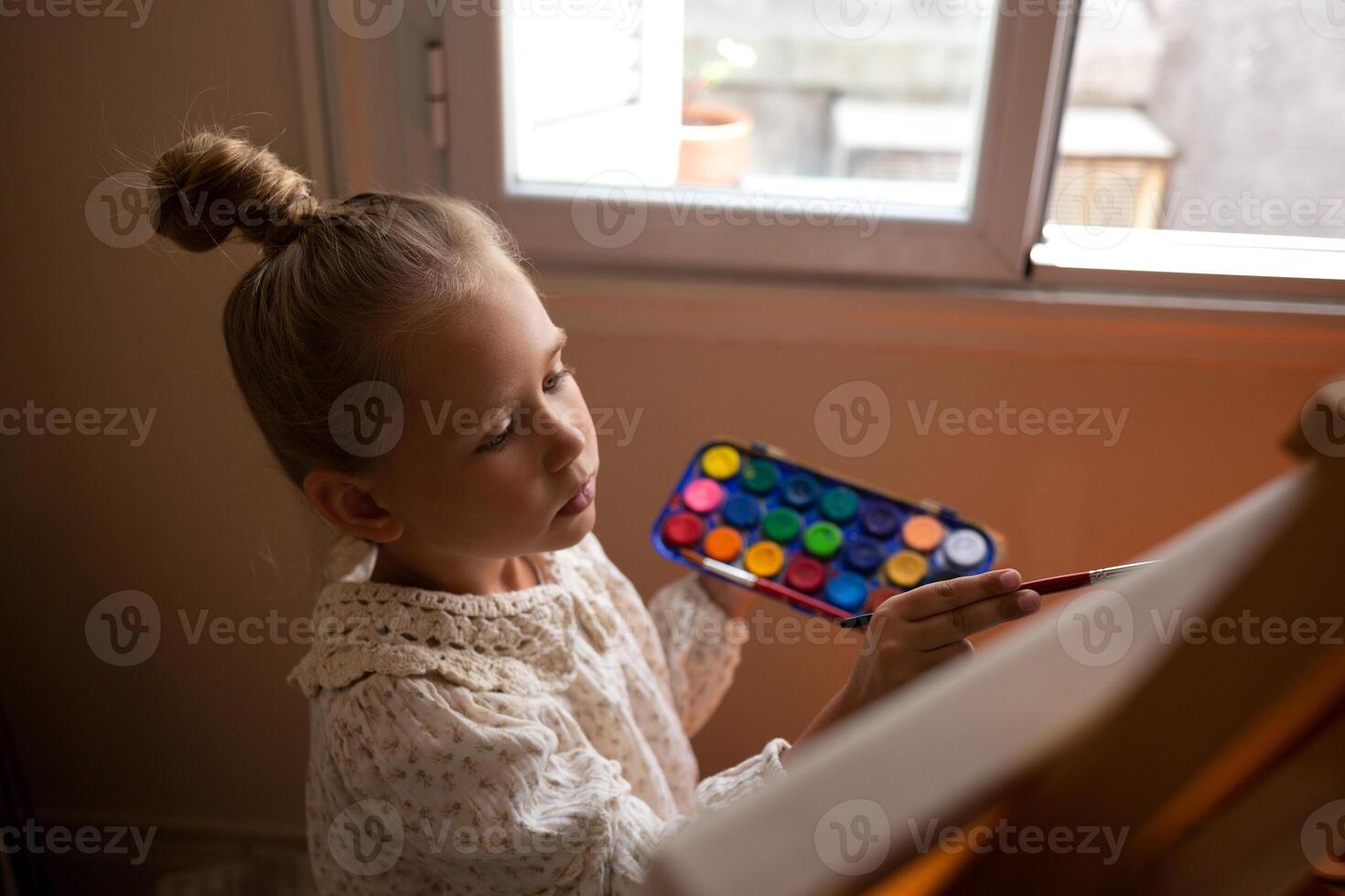 little cute girl draws with paints on canvas at the easel photo