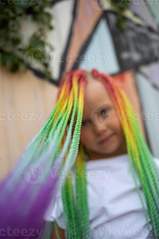 portrait of a little beautiful girl with multi-colored african braids on the background of a colorful wall photo