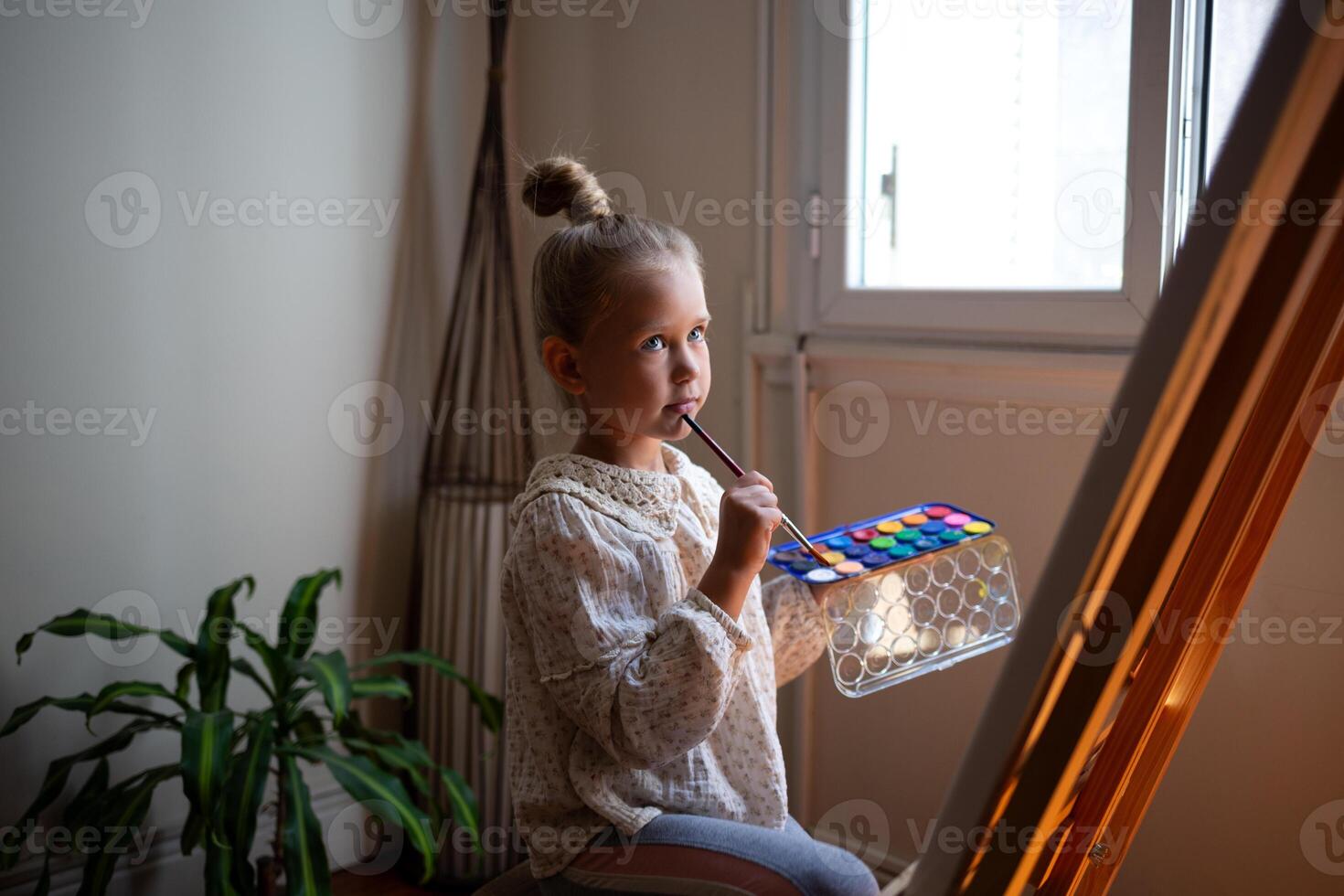 little cute girl draws with paints on canvas at the easel photo