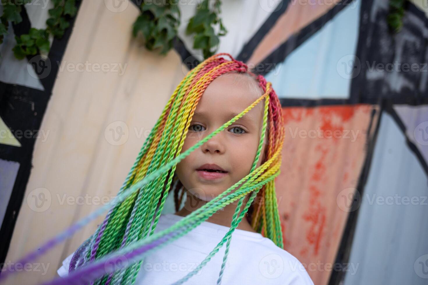 portrait of a little beautiful girl with multi-colored african braids on the background of a colorful wall photo