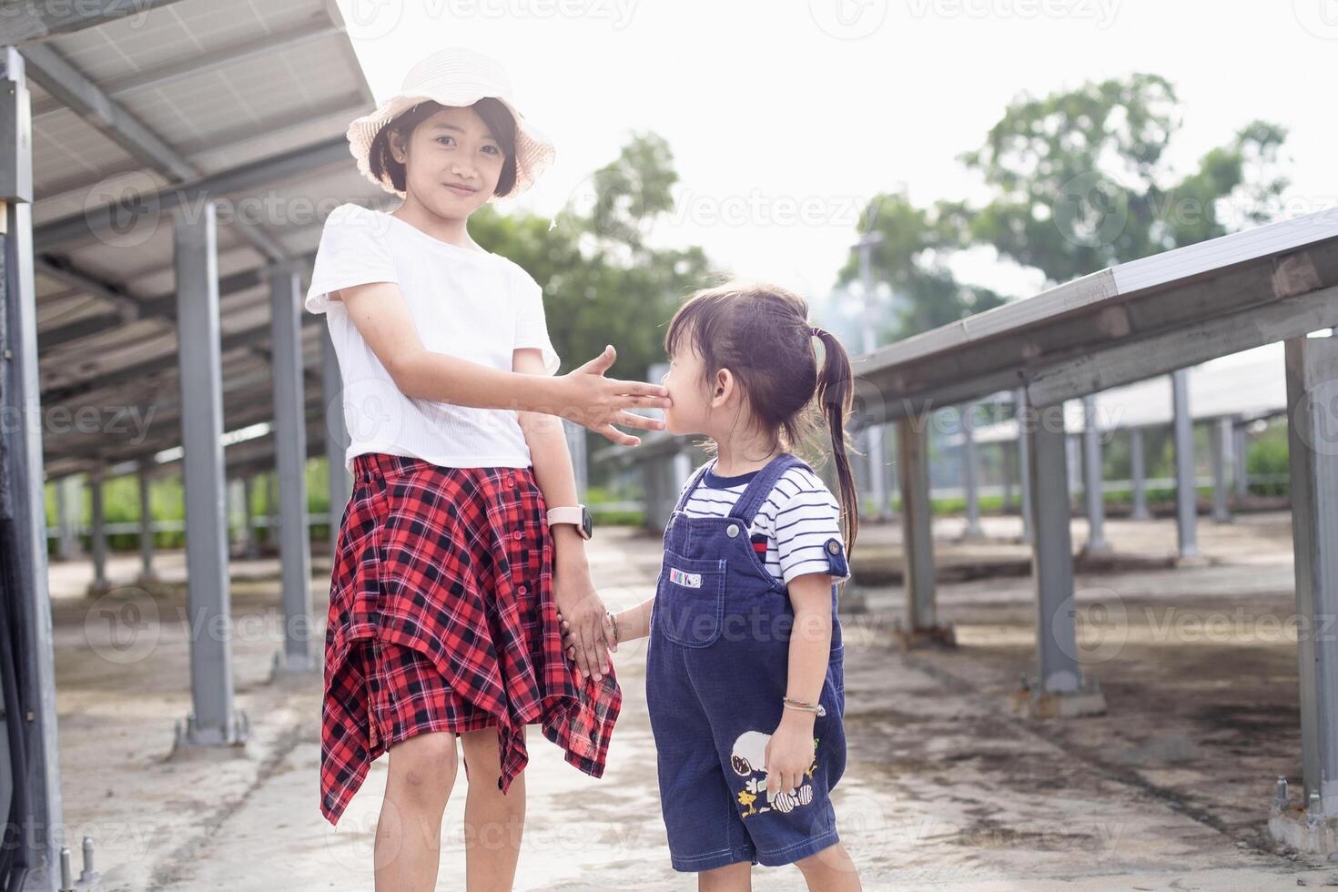 Two cute little girls have fun playing on a solar cell farm, standing in front of solar panels. photo