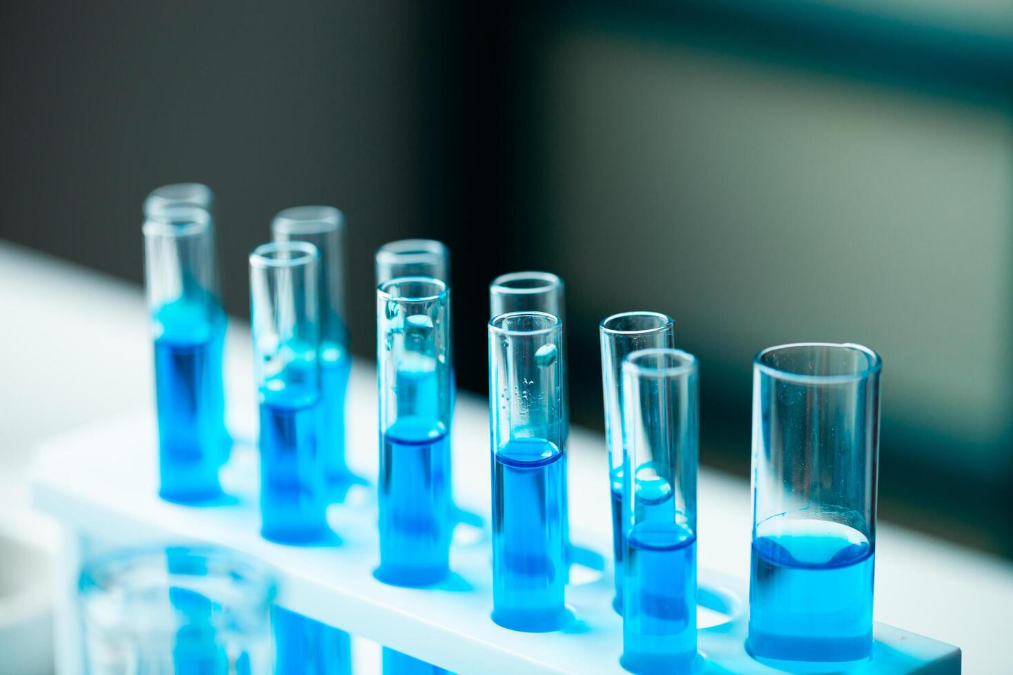 A row of blue test tubes are lined up on a white lab bench. The tubes are filled with clear liquid, and the overall mood of the image is one of scientific experimentation and discovery photo