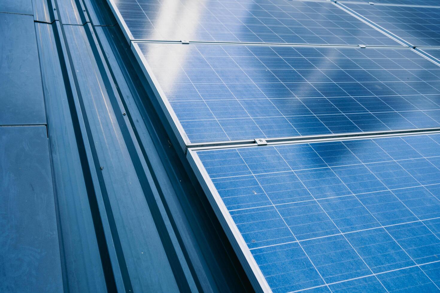 A solar panel is shown in the image, with a blue and silver color scheme. The panel is installed on a roof, and it is a large, multi-panel system photo