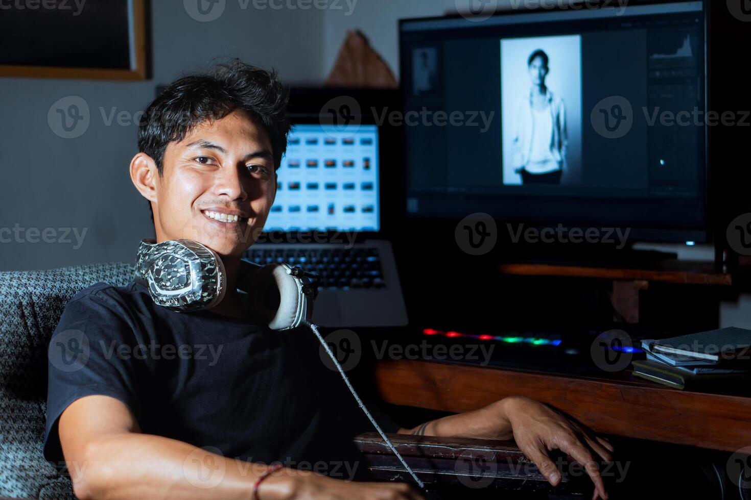Young man smiling at desk with computer and headphones photo