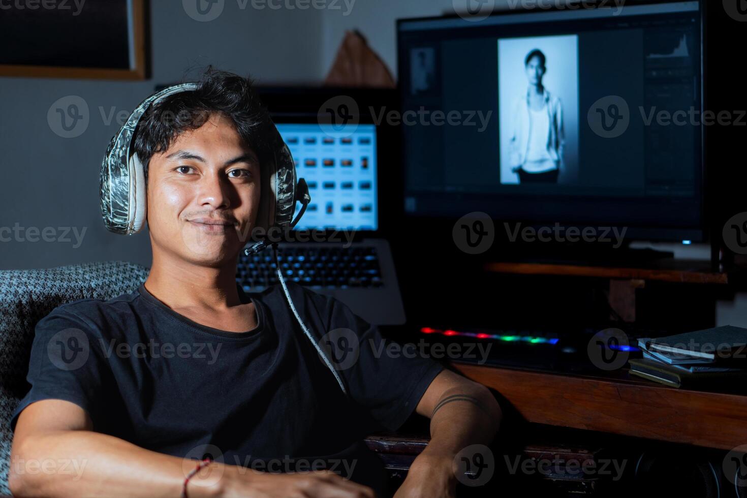 Young man smiling at desk with computer and headphones photo