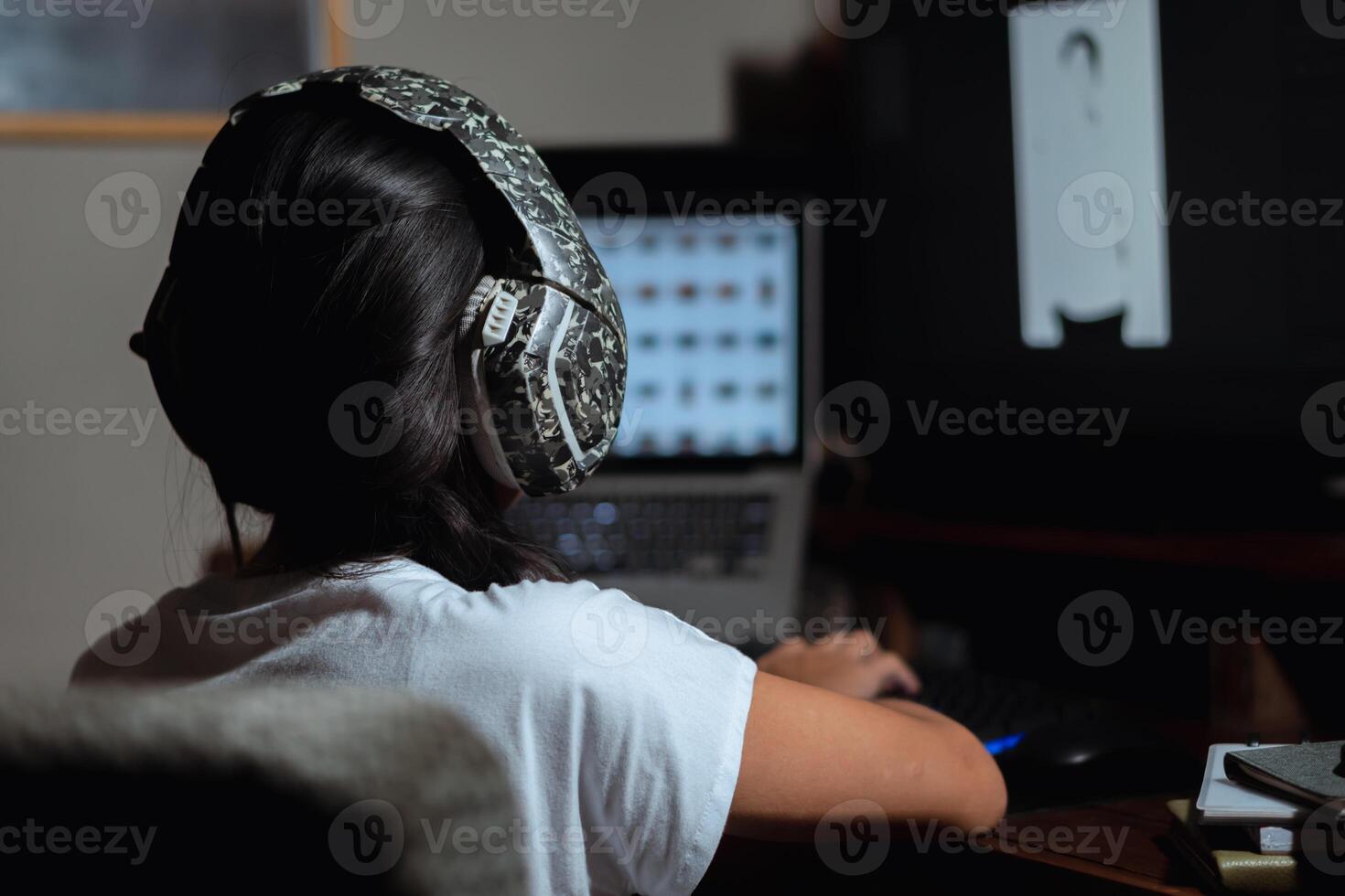Person working on a computer with headphones in a dimly lit room photo