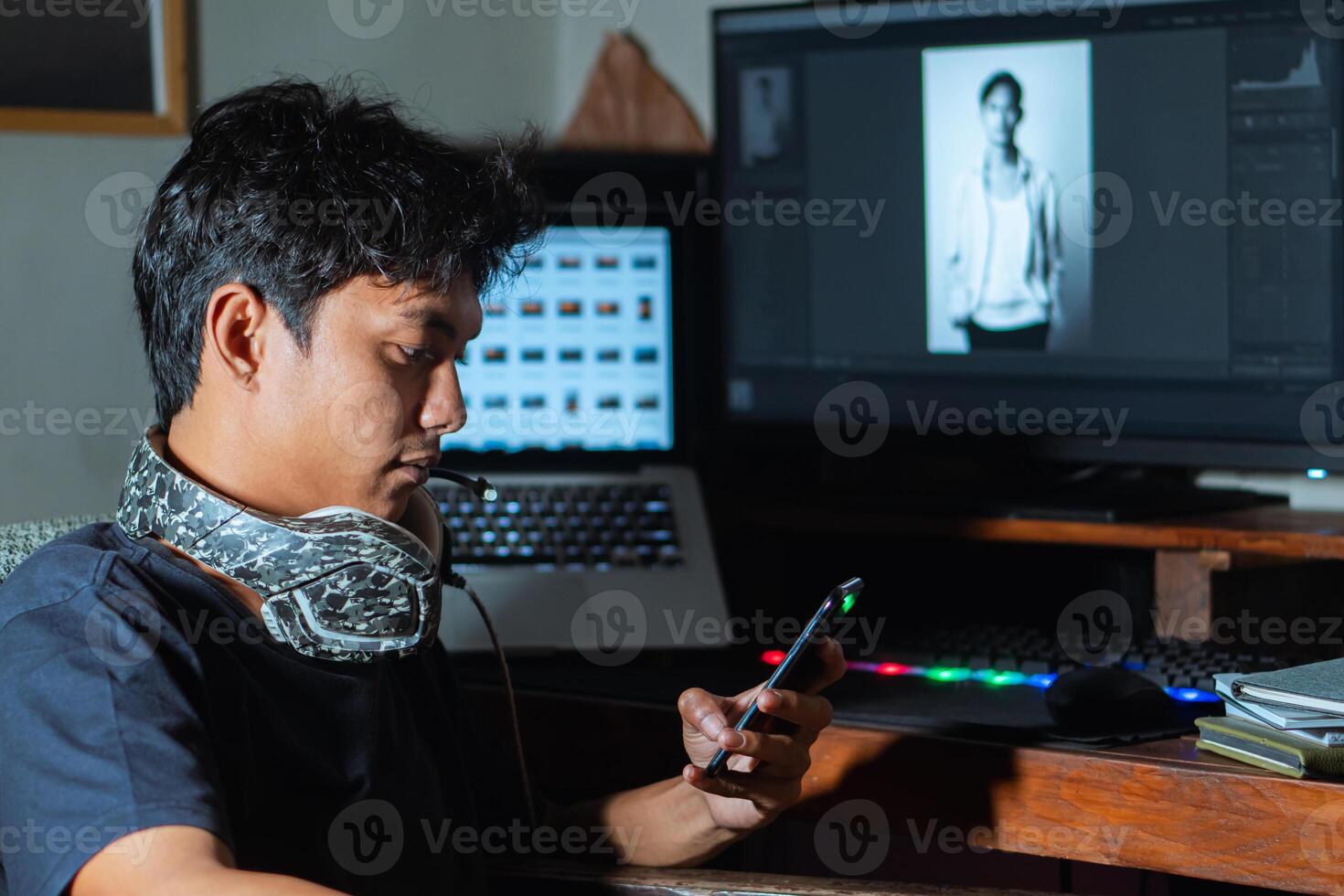 Young man using phone at desk with laptop and monitor photo
