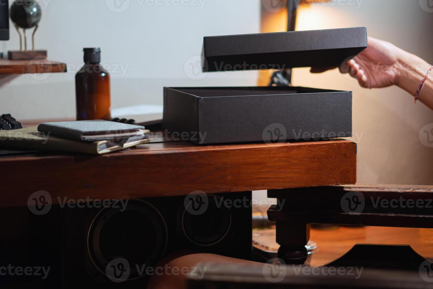 Person opening a black gift box on a wooden desk photo